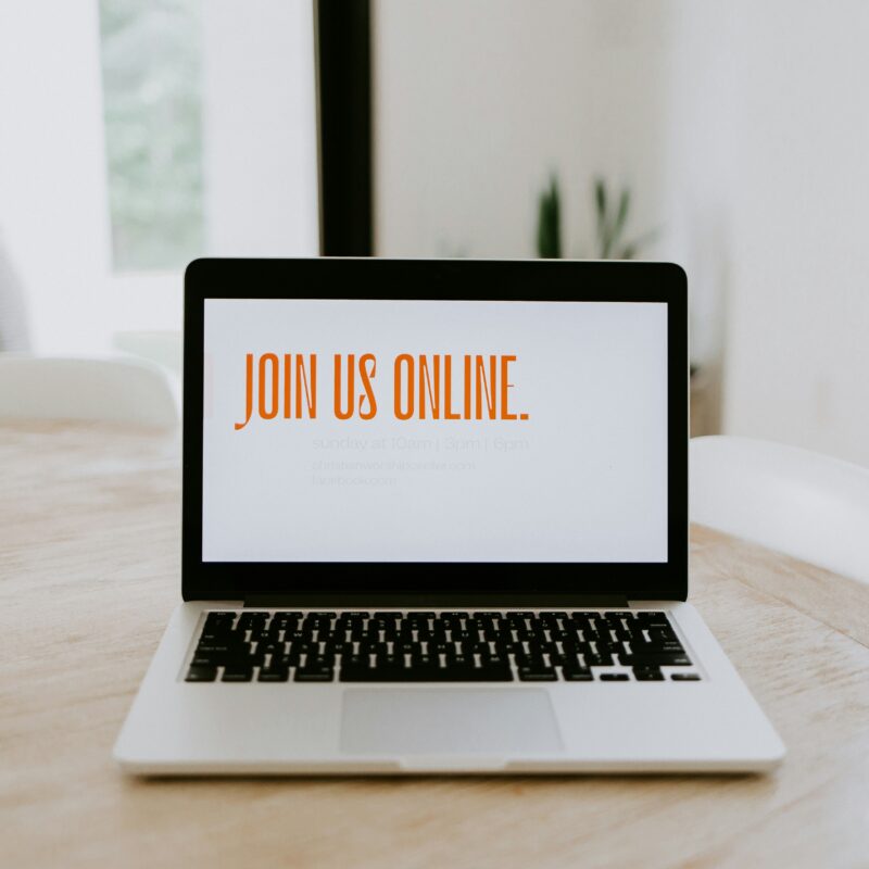 View of a laptop in a table top, with the words Join Us Online written on the laptop screen to hint at selling in your sleep via online courses